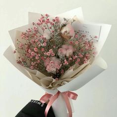 a bouquet of flowers is wrapped in paper and tied to a black bag with pink ribbon