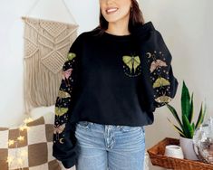 This beautiful Luna Moth sweatshirt with the phrase "find light in the dark" has a gorgeous sleeve print on both sleeves, with dark celestial nature vibes. Our crewneck sweatshirts have a loose fit and are made with a medium-heavy cotton/poly blend making them warm, comfortable, and cozy. There are no itchy side seams and the collars are ribbed knit, so they retain their shape even after washing. SPECIFICATIONS ❤️ Unisex sizing ❤️ Medium-heavy cozy fabric ❤️ Sewn-in label ❤️ Loose fit, size up for an oversized look ❤️ 50% cotton, 50% polyester ❤️ Colors may slightly vary due to monitor differences PRINTING PROCESS We use direct-to-garment printing, a much more sustainable method than older printing methods, like screen printing. We apply pigmented water-based inks that are absorbed by the Aesthetic Long Sleeve Sweatshirt For Fall, Goblincore Sweater, Dark Celestial, Granola Girl Aesthetic, Nature Vibes, Dark Cottagecore, Aesthetic Nature, Luna Moth, Granola Girl