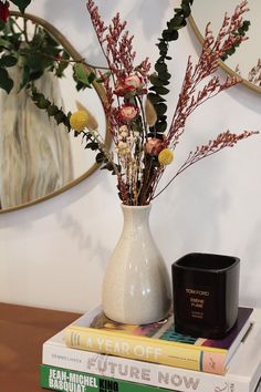 a vase filled with flowers sitting on top of two books next to a candle and mirror