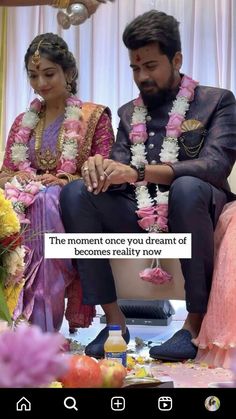 a man and woman sitting next to each other in front of a flower arrangement on the ground