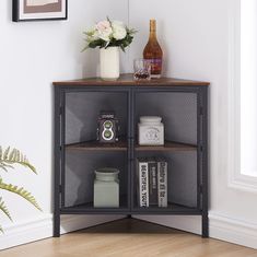 a corner shelf with books and bottles on it next to a vase filled with flowers