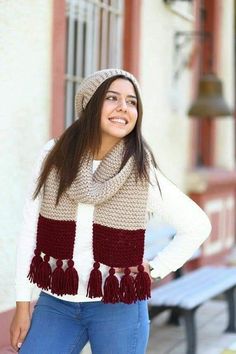 a woman standing in front of a bench wearing a hat and scarf with tassels