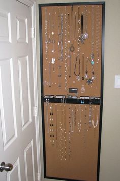 a wall mounted jewelry rack in the corner of a room with a door open to reveal an assortment of necklaces on display