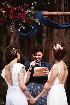 a man standing next to two women in front of a tree holding a piece of paper