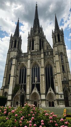 the large cathedral has many windows and spires on it's sides, with pink flowers in front