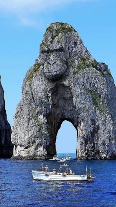 a boat is in the water near an arch shaped rock formation that looks like it's coming out of the ocean