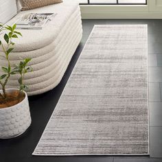 a white rug on the floor next to a couch and potted plant in front of a window