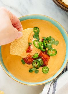 a hand dipping a tortilla chip into a bowl of quesadilla soup