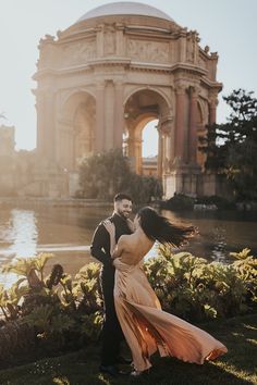 a man and woman standing next to each other in front of a building with water