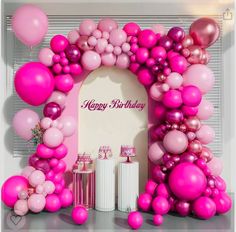 a pink birthday party with balloons and streamers in the shape of an arch,