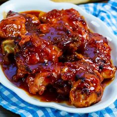 a white bowl filled with chicken wings covered in bbq sauce on top of a blue and white checkered cloth