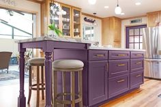 a kitchen with purple cabinets and stools next to a counter top in front of a window