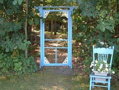 a blue chair sitting in the middle of a garden next to a wooden arbor with flowers on it