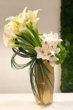 a gold vase with white flowers in it on a table next to a green plant