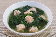 a white bowl filled with meatballs and spinach in broth on top of a table