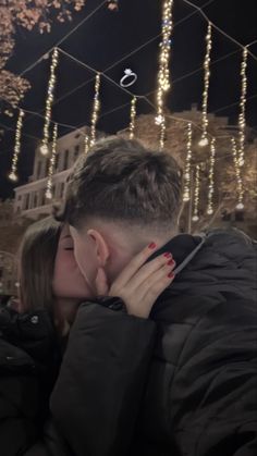 a man and woman kissing in front of christmas lights on the side of a building