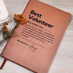 a brown book with the words best volunteer written on it next to some flowers and napkins