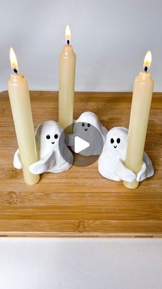 three candles sitting on top of a wooden table next to two ghost figurines