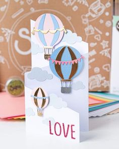 a card with hot air balloons and the word love written in pink, blue, and white