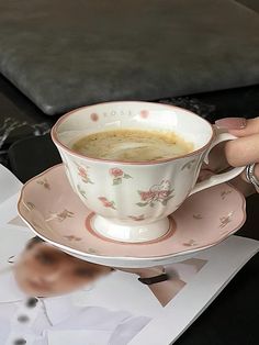 a woman is holding a coffee cup and saucer on a table next to photos