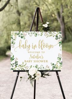 a welcome sign for a baby shower with flowers on it and greenery in the background