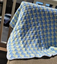 a blue and white crocheted blanket sitting on top of a wooden chair next to a window