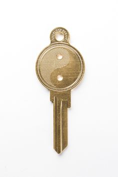 a gold key with a yin symbol on the front and back of it, against a white background