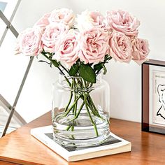 some pink roses are in a glass vase on a table next to a framed print