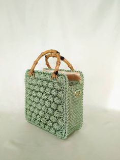 a green crocheted bag sitting on top of a white table next to a wooden handle