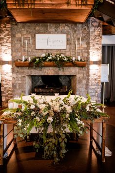 a table with flowers and greenery on it in front of a fire place at a wedding