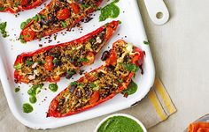 several stuffed peppers on a white platter with pesto and seasoning next to it