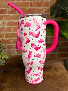 a pink and white travel mug sitting on top of a table next to a brick wall