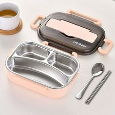 a lunchbox with compartments and spoons next to it on a white countertop