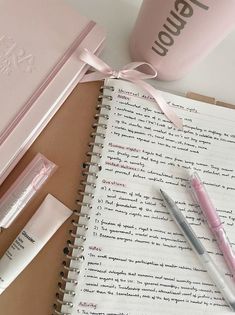 an open notebook with pink writing on it next to a pen and two empty lip bales