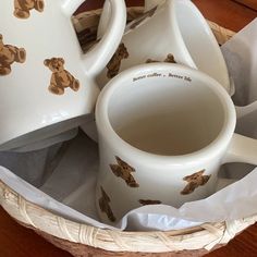 a basket filled with white and brown teddy bears on it's sides next to two mugs