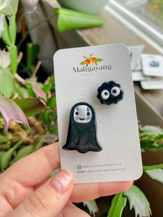 a pair of black and white ghost earrings on a card next to some green plants