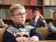 two boys sitting in front of bookshelves with one boy wearing glasses looking at the camera