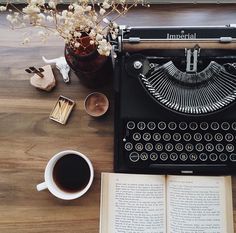 an old fashioned typewriter sitting on top of a wooden table next to a cup of coffee