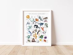 an ocean alphabet poster hanging on the wall in front of a white wall with wood flooring