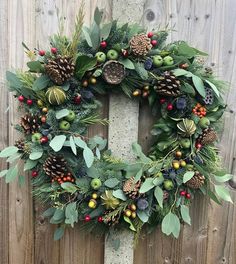 a christmas wreath hanging on the side of a wooden fence with pine cones and berries