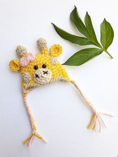 a crocheted giraffe hat next to a green leaf on a white surface