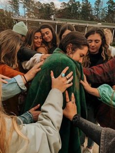 a group of people standing around each other with their arms wrapped in a green blanket