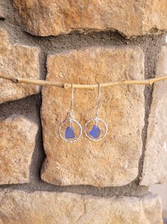 the earrings are hanging on a rope near a stone wall with a rock in the background