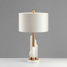 a table lamp with a white shade on it and a gold plated metal base