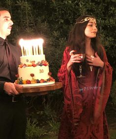 a man and woman standing next to each other holding a cake with candles on it