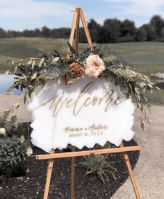 a welcome sign sitting on top of a wooden easel with flowers and greenery