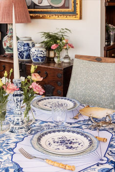 a blue and white table setting with flowers in vases on the dining room table