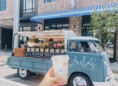 a person holding up a drink in front of an old truck with flowers on it