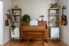 a room with a piano, bookshelf and plants on the wall next to it