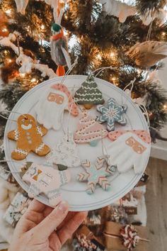 a person holding up a plate with cookies on it in front of a christmas tree